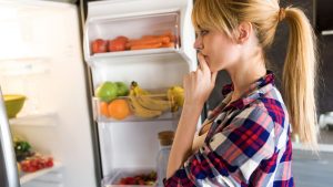 A woman wonders, "Why is my refrigerator not cooling?" while standing at her appliance.