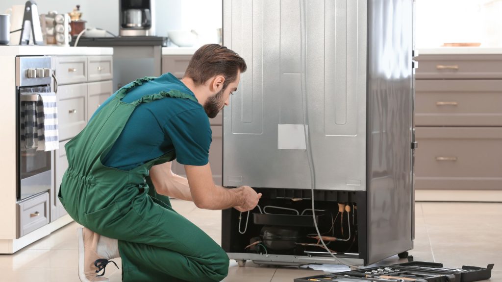 A technician fixes his fridge while wondering, "Why is my refrigerator not cooling?" 