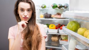 A woman stands in front of her appliances and wonders about the reason behind her refrigerator not cooling.
